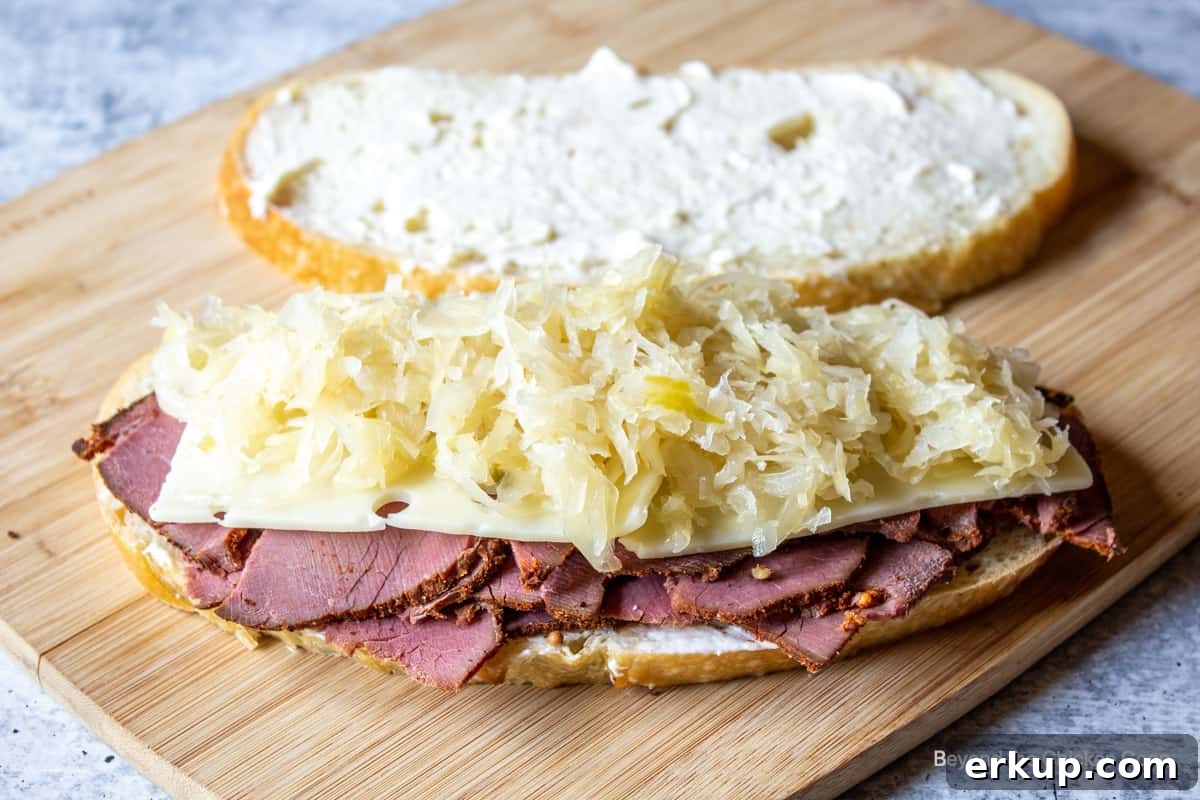 Making a sandwich with pastrami, cheese and sauerkraut.