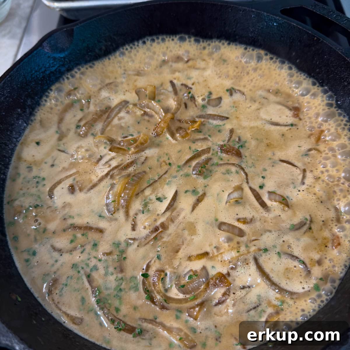 A sour cream onion sauce cooking down on the stovetop in a cast iron pan. 
