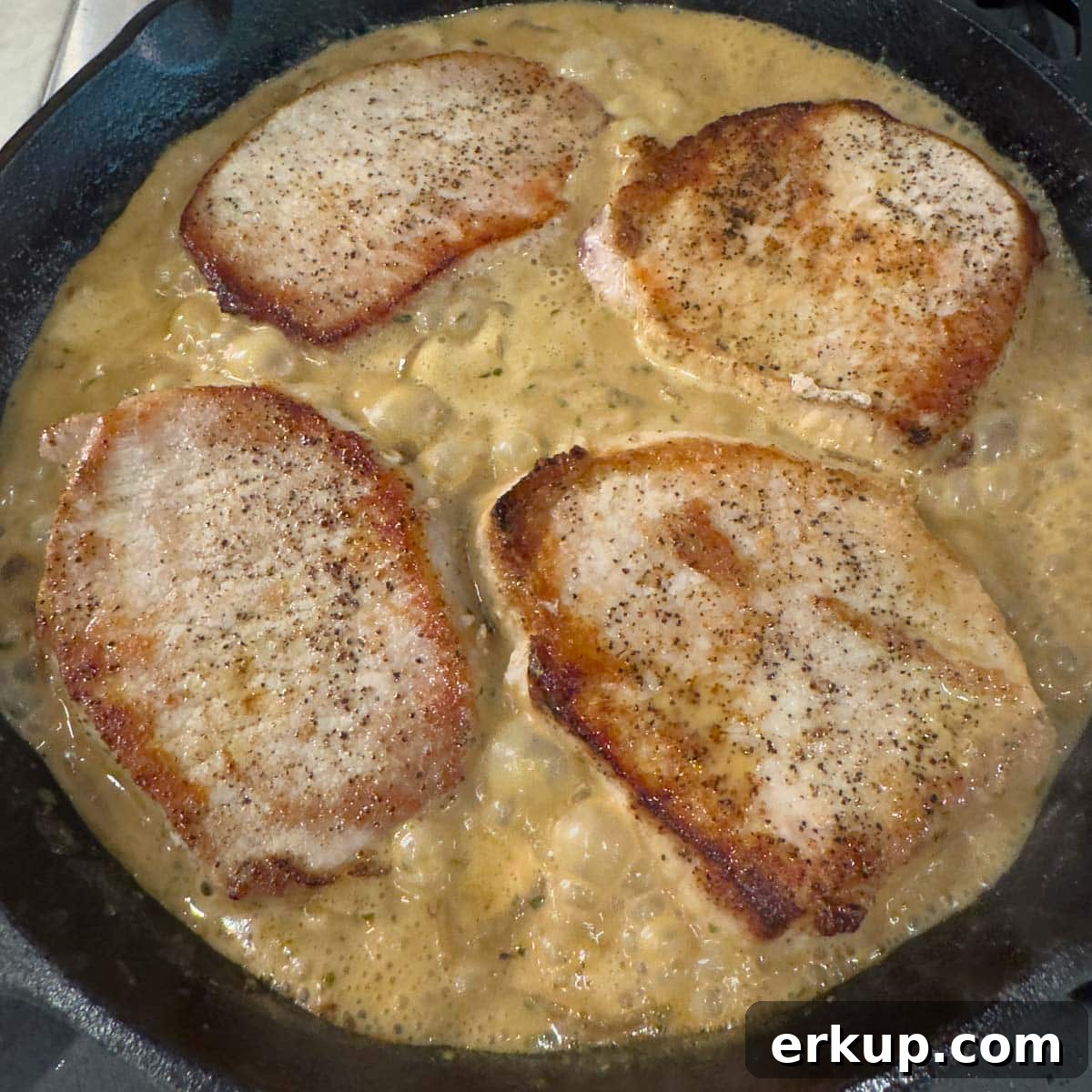Boneless pork chops in a black skillet on top of sauce to be cooked down.