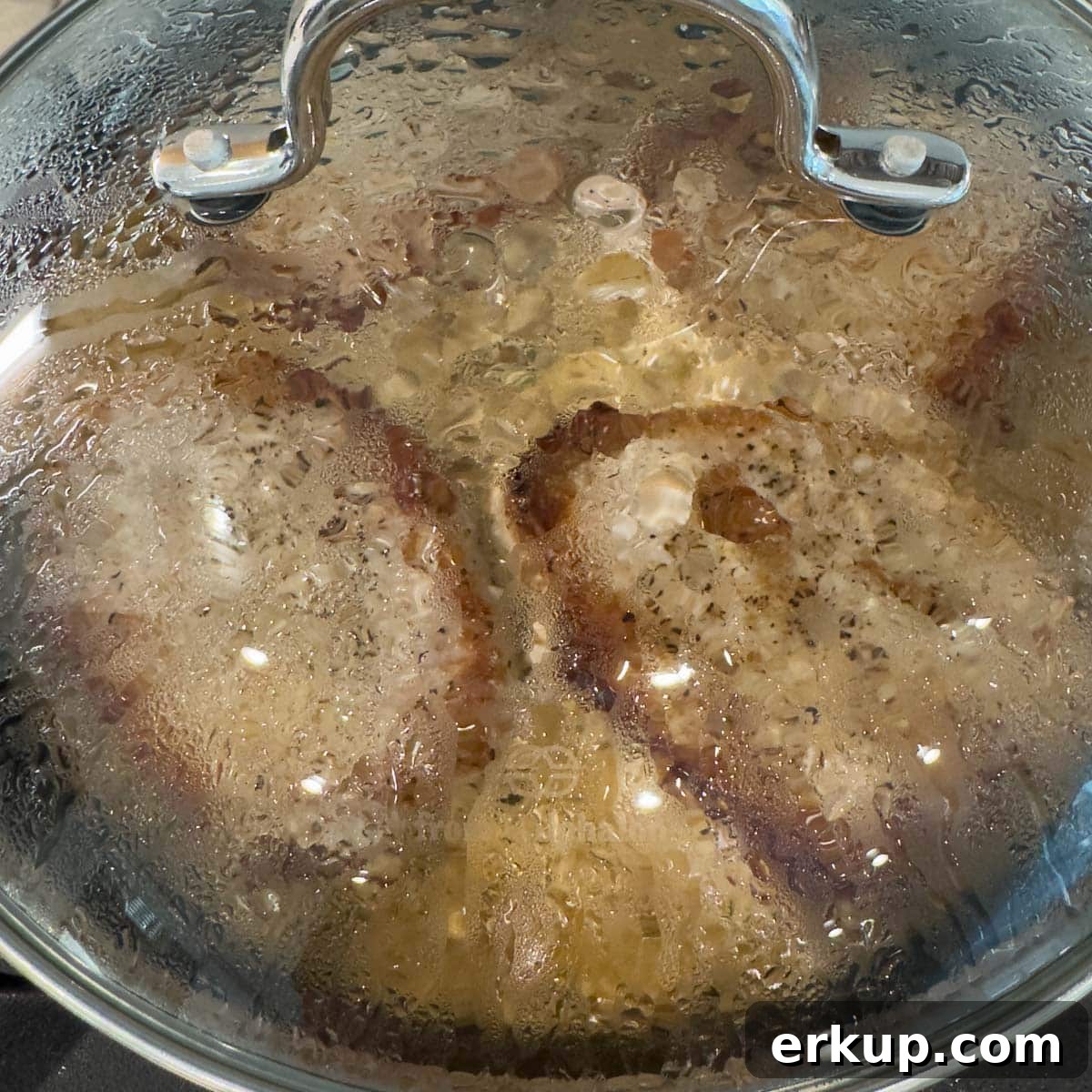 Pork chops under a glass lid to finish cooking on the stovetop.