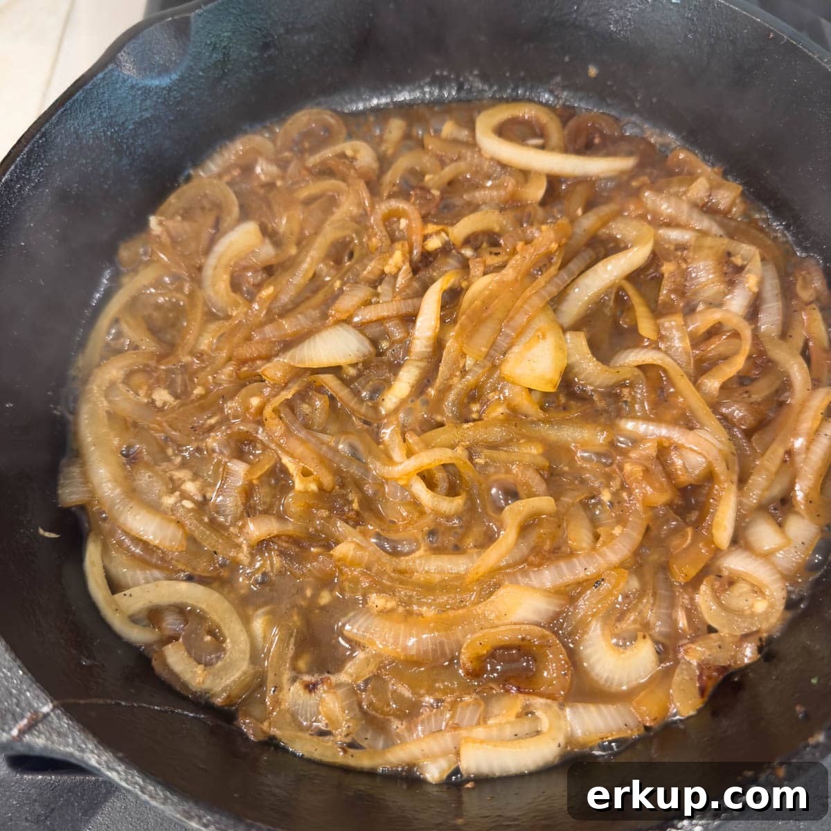 Golden brown caramelized onions in a black skillet deglazing with wine.