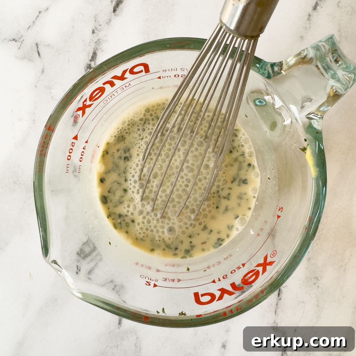 Sauce ingredients being whisked together in a pyrex glass measuring cup.