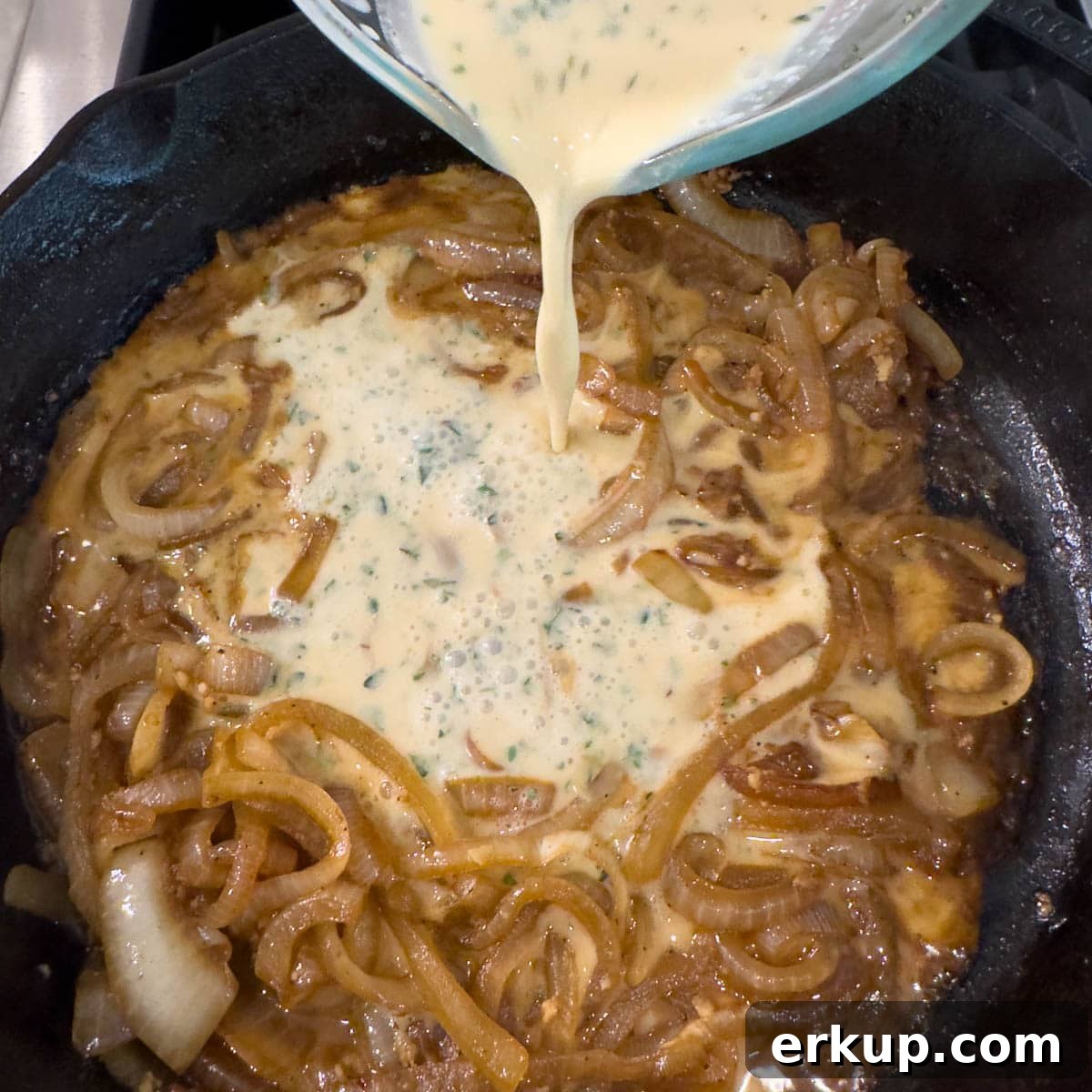 Creamy sauce mixture pouring into a pan of caramelized onions to make a sauce.