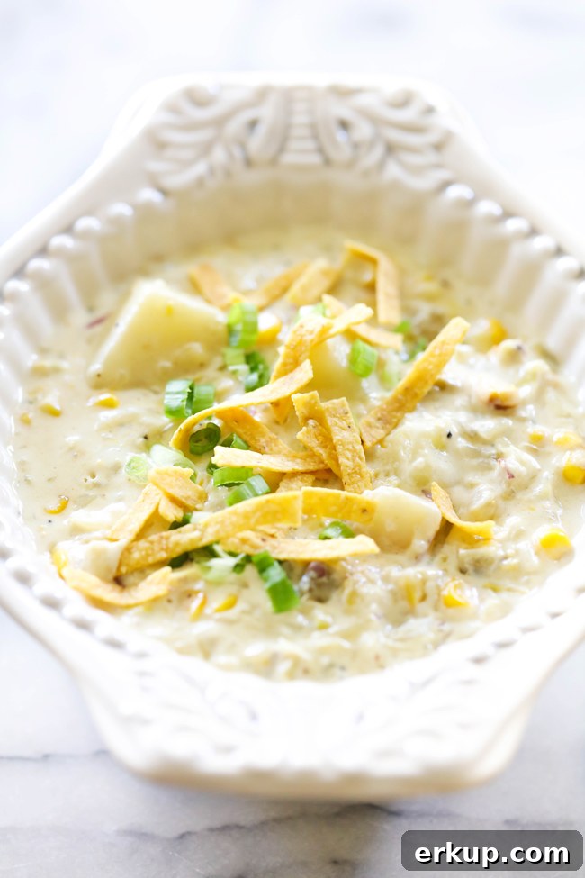 Green Chile Potato Soup in white bowl garnished with sliced green onions and tortilla chips.