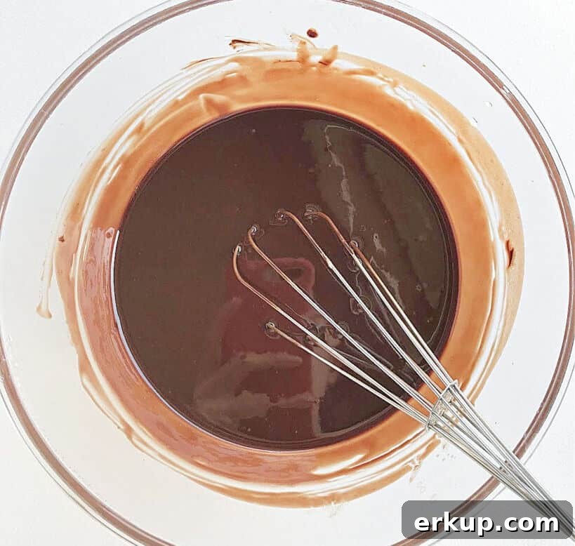 Glass bowl with melted chocolate and butter. A wire whisk. White background.