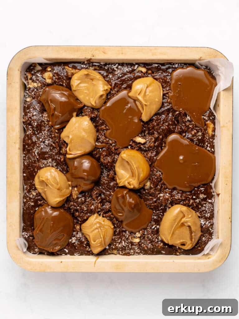 Peanut butter and dulce de leche mounds on top of brownie batter in pan. White background.