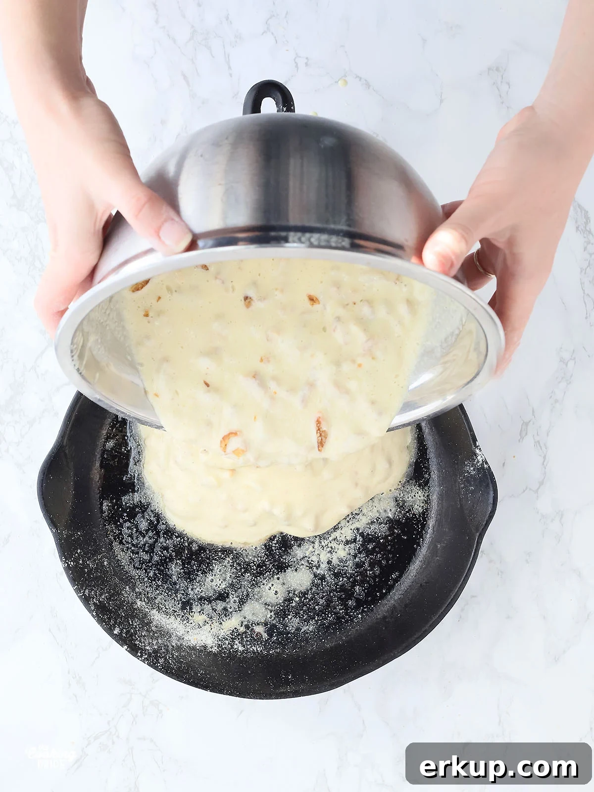 hands pouring cracklin' corn bread batter into a cast iron skillet
