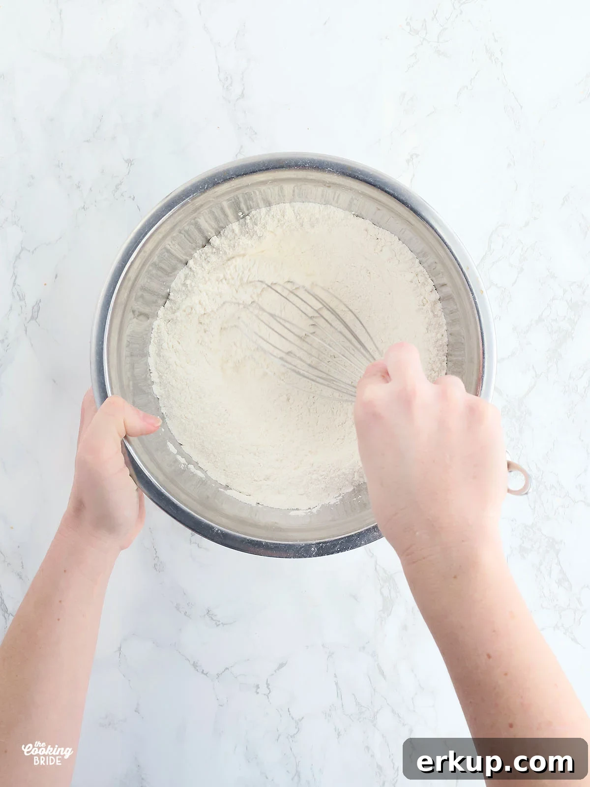 hand whisking dry corn bread ingredients together in a stainless steel mixing bowl