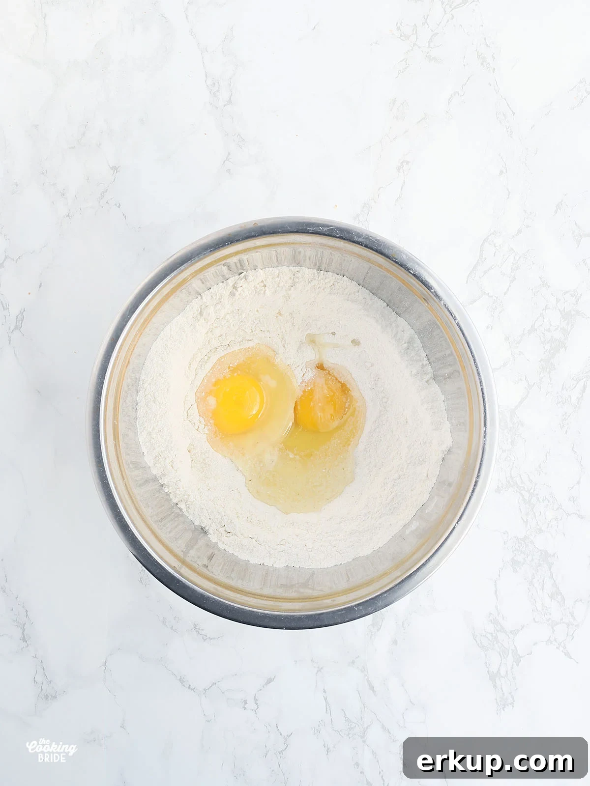 stainless steel bowl with dry corn bread ingredients and two eggs
