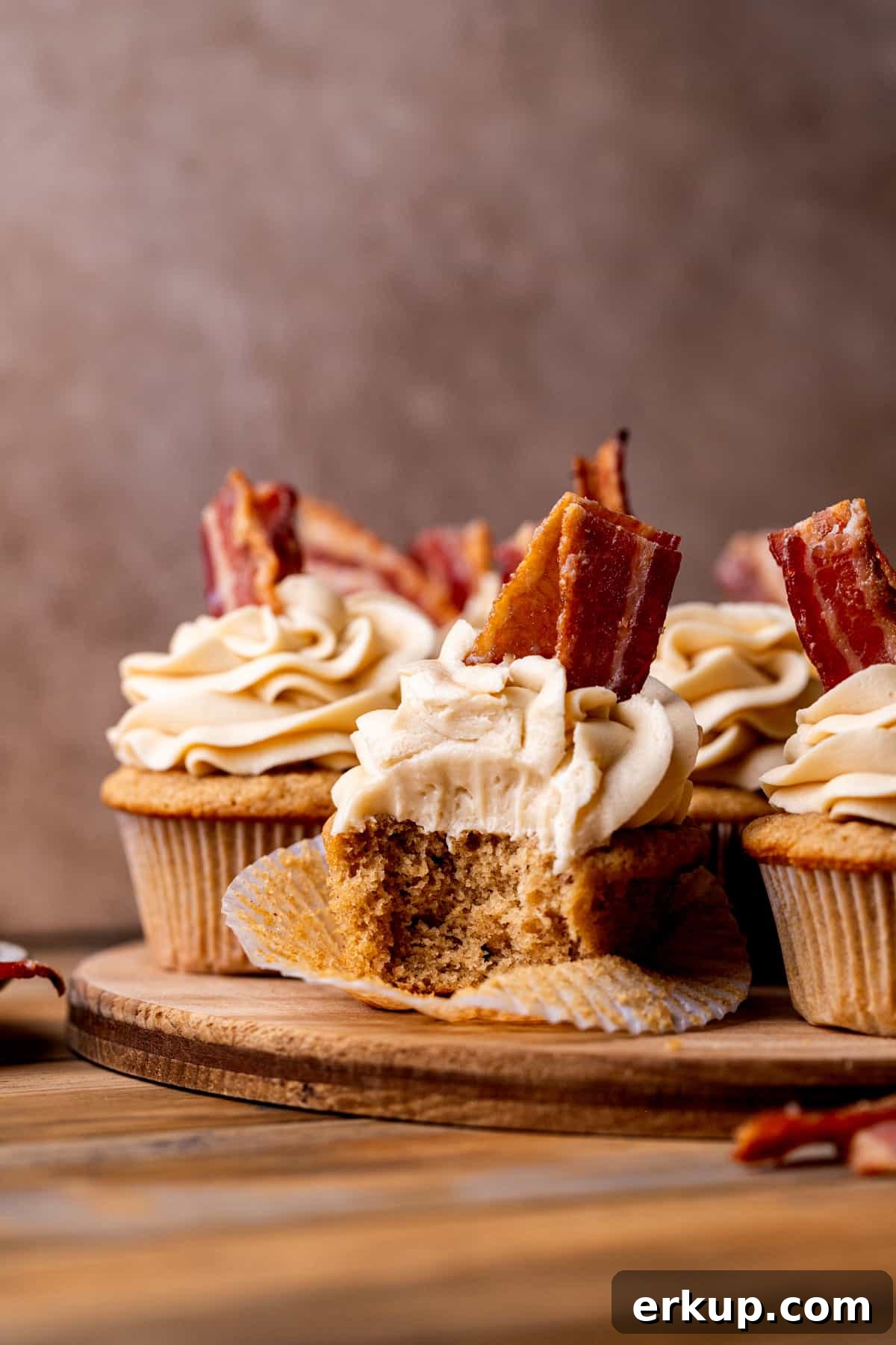 Maple Bacon Cupcakes with Candied Bacon 3 Cupcakes on a wood baord.