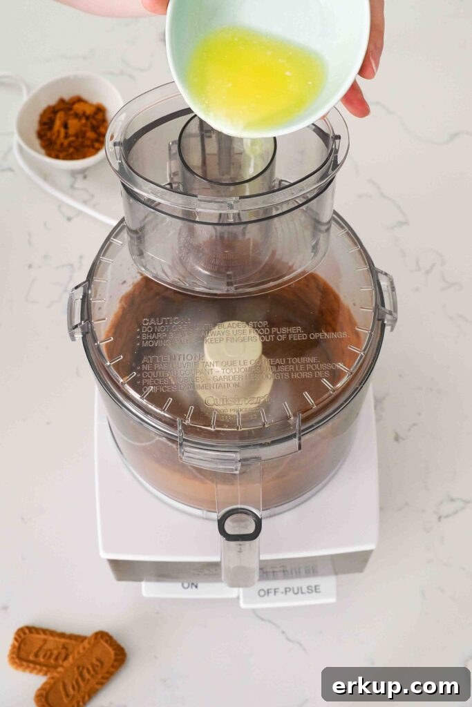 Melted butter is poured into a food processor bowl with Biscoff cookies.