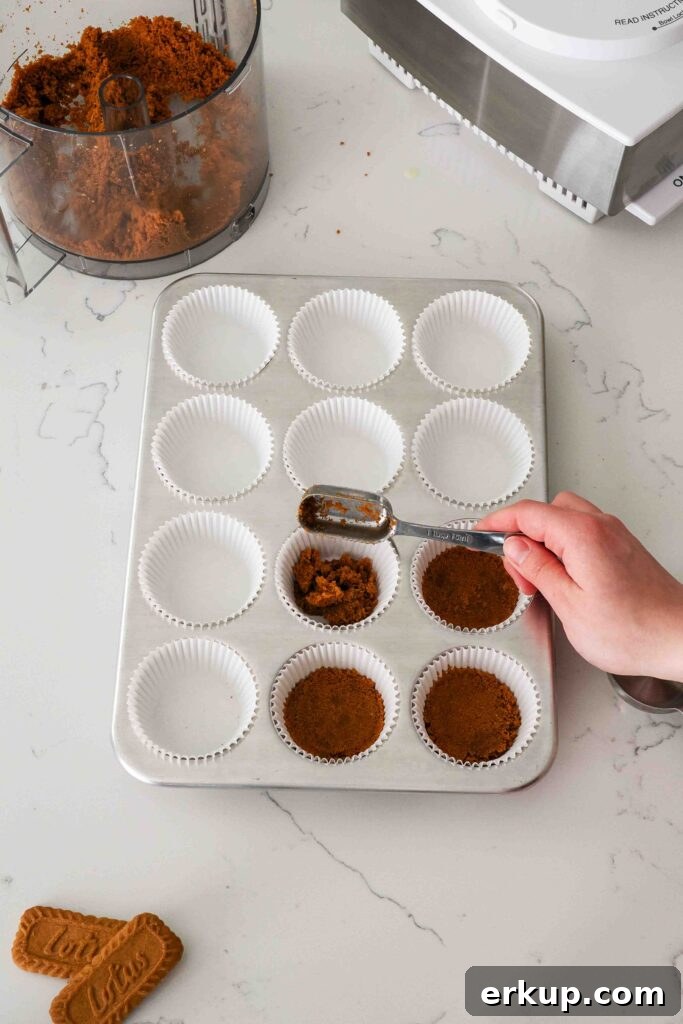 A hand adds cookie crumbs to paper liners in a muffin pan.