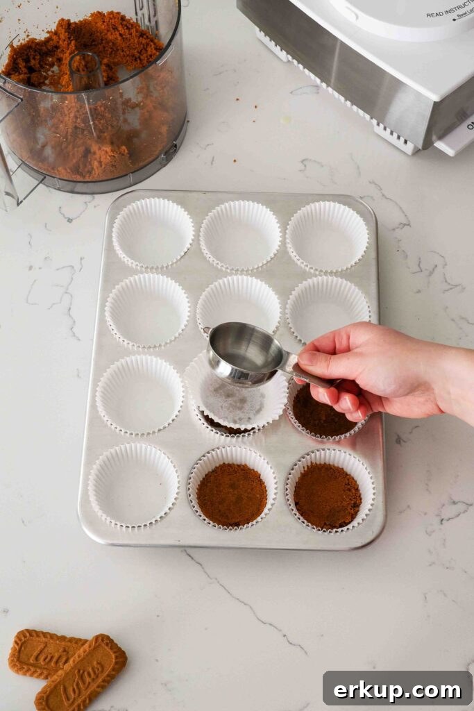 A hand uses a measuring cup to flatten cookie crusts in a muffin pan.