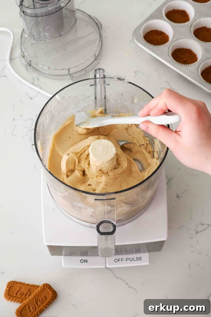 A spatula scrapes down the side of a food processor bowl with Biscoff cheesecake filling on the sides.