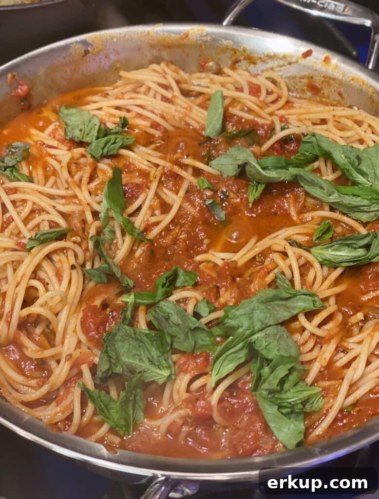 Large skillet of spaghetti tossed with tomato basil sugo recipe and fresh basil leaves.