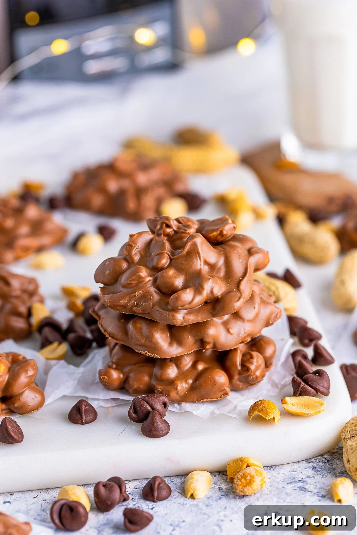 Three stacked Slow Cooker Peanut Clusters with chocolate chips and peanuts around them.
