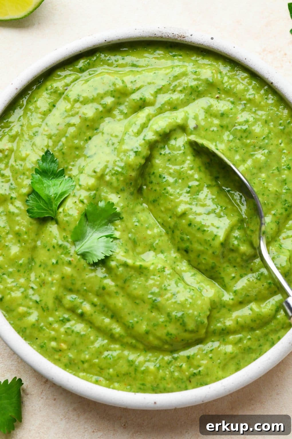 A spoon dipping into a small bowl of bright green avocado herb green sauce.