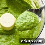 How to make avocado herb green sauce: A spoon lifting out a small amount of sauce from the food processor to show the creamy texture.