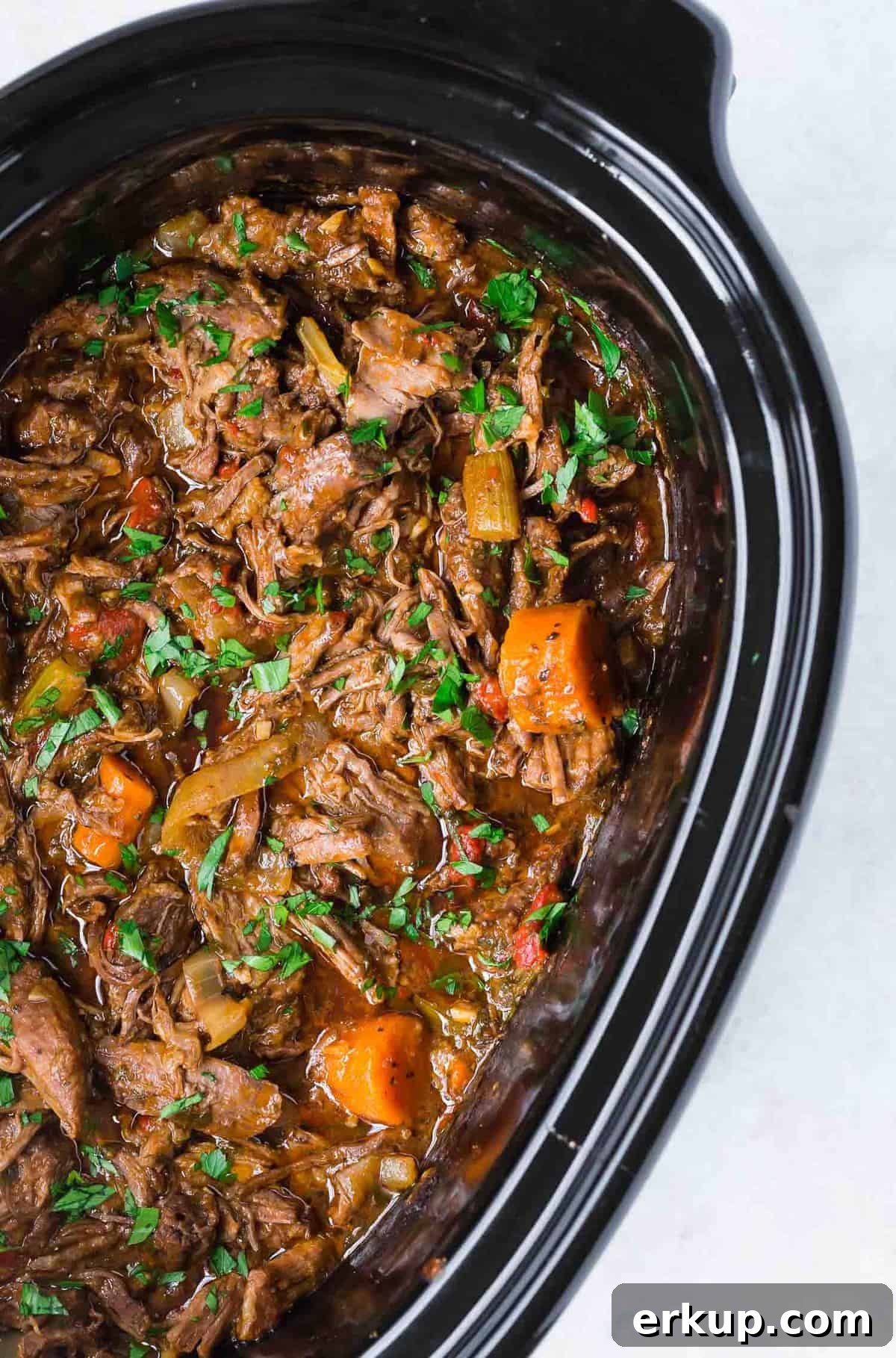 Pot roast and carrots in a black slow cooker.