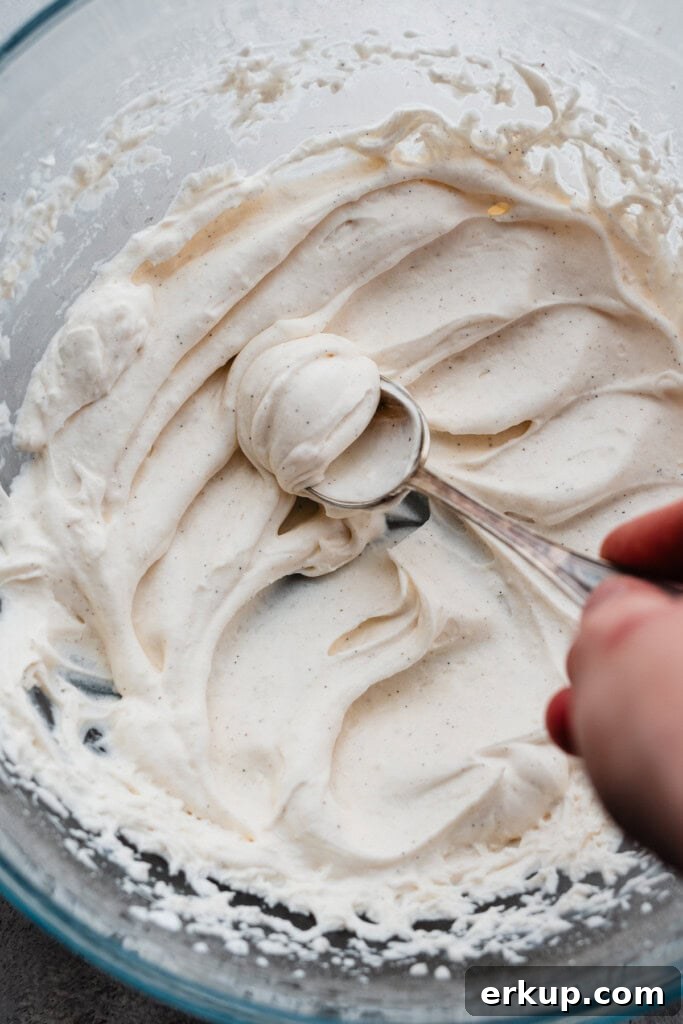 A spoon being pushed through the swoops of whipped cream to make a beautiful dollop.