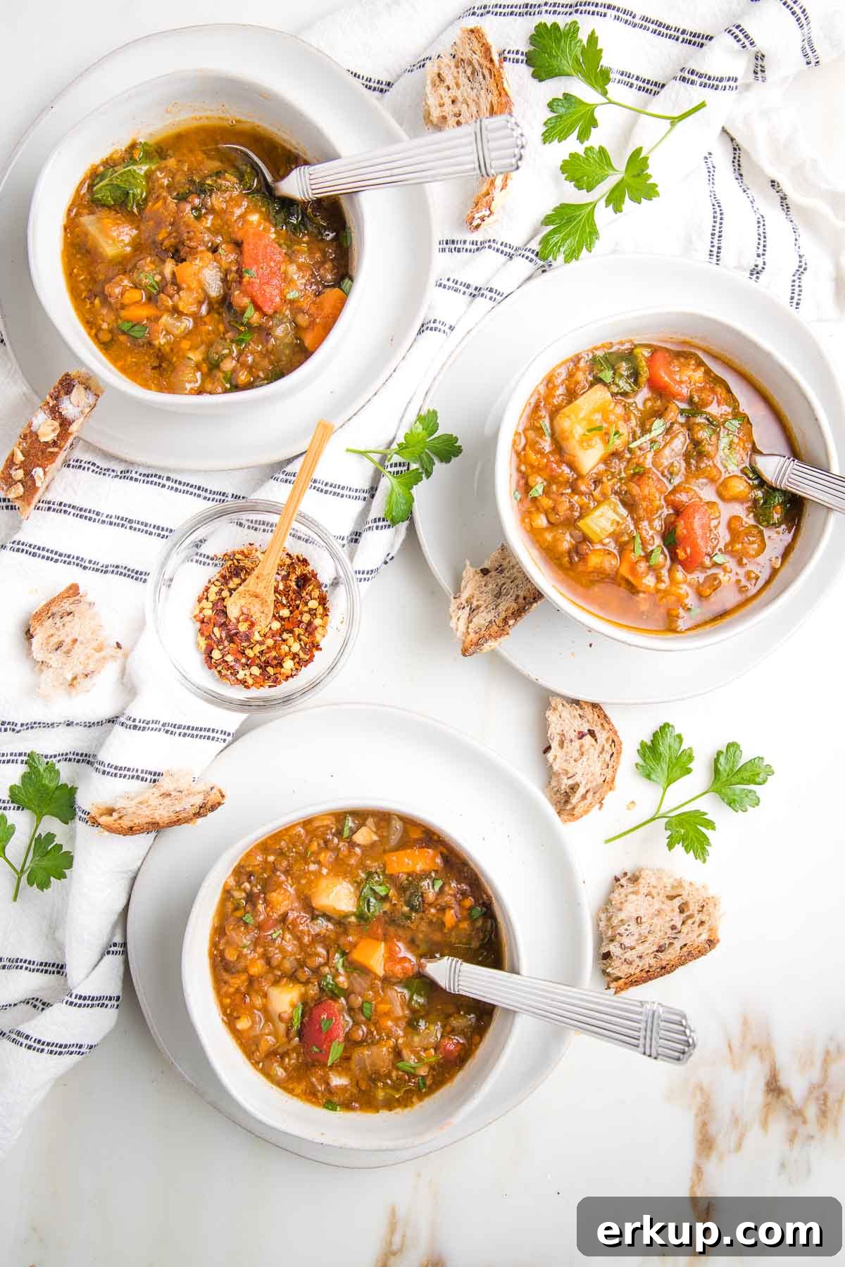Bowls of chunky lentil soup with crusty bread, fresh parsley and a dish towel.