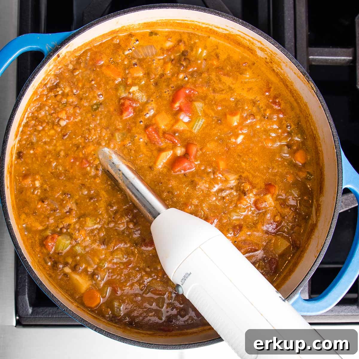Immersion blender in the center of a dutch oven filled with chunky vegan lentil soup