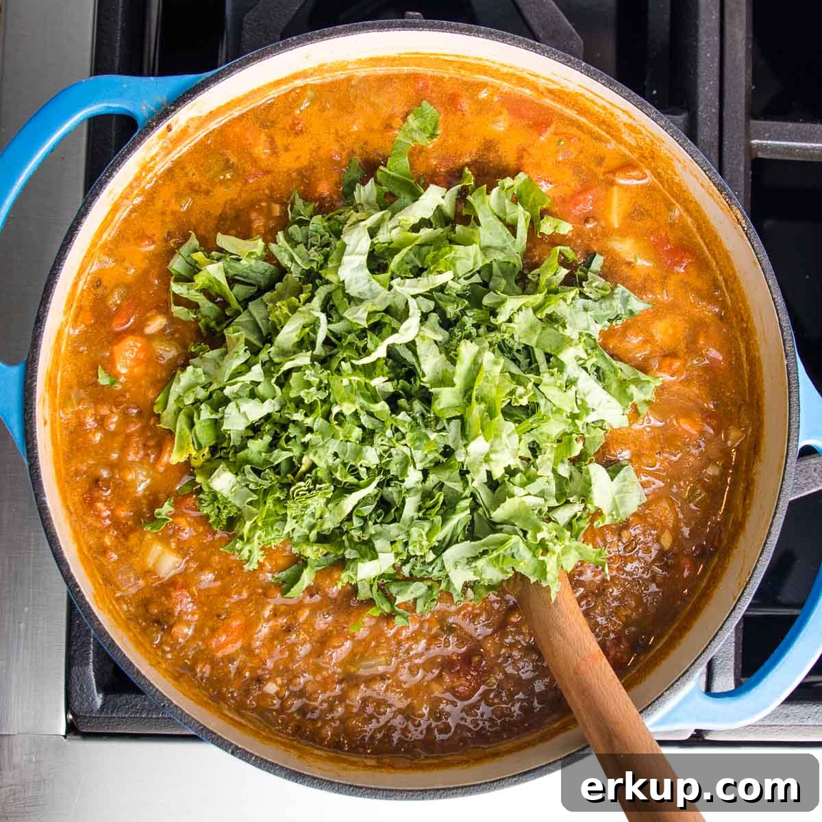 Dutch oven filled with lentil soup and a large pile of kale on top.