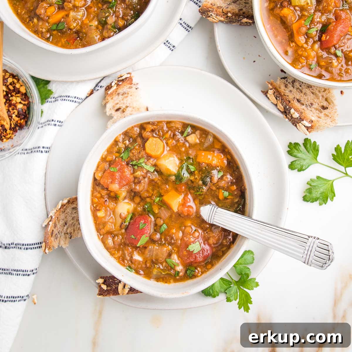 Chunky vegetable lentil soup in bowls with crusty bread pieces on the side.