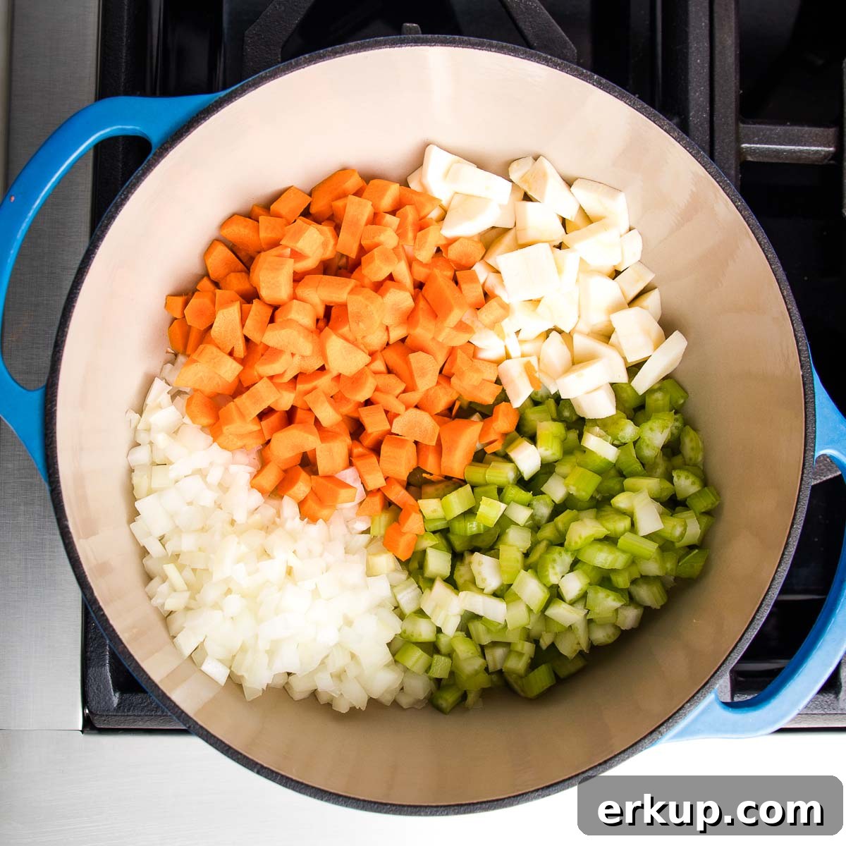 Dutch oven filled with sections of diced carrots, onions, celery and parsnips. 