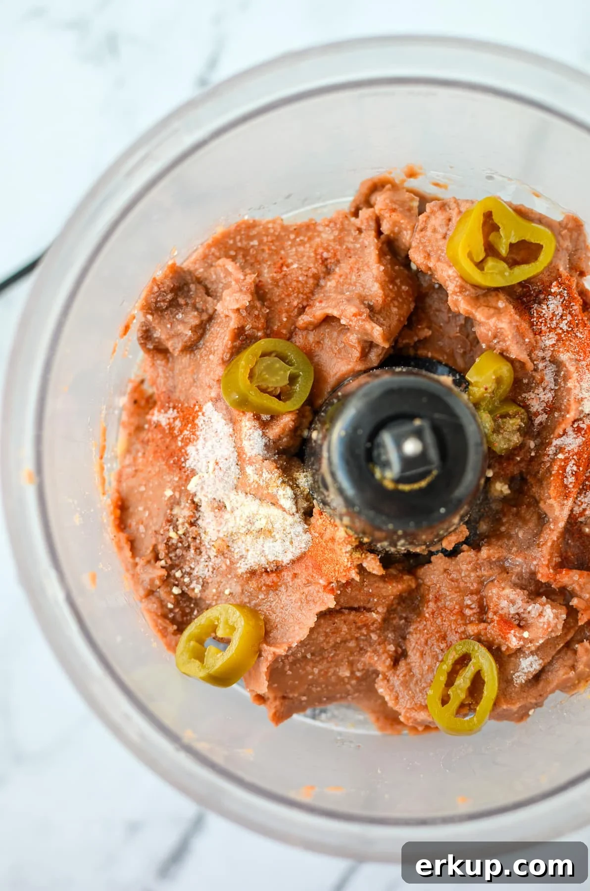 A food processor with refried beans, jalapeno slices, and seasonings.