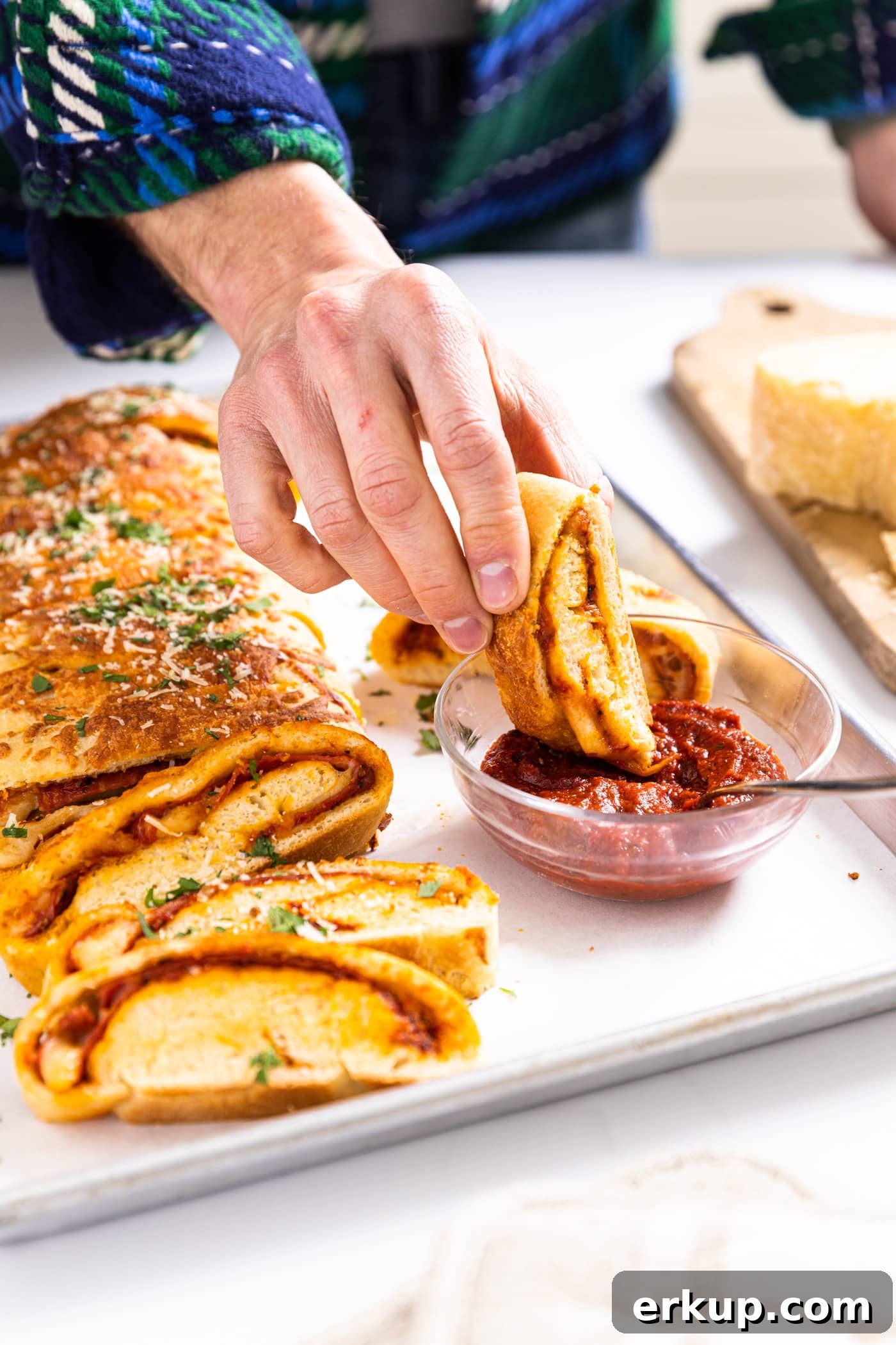 Homemade Stromboli Recipe: Crispy Cheesy Italian Roll 4 Hand dipping slice of stromboli into red tomato sauce sitting in small glass bowl with rest of stromboli sitting beside