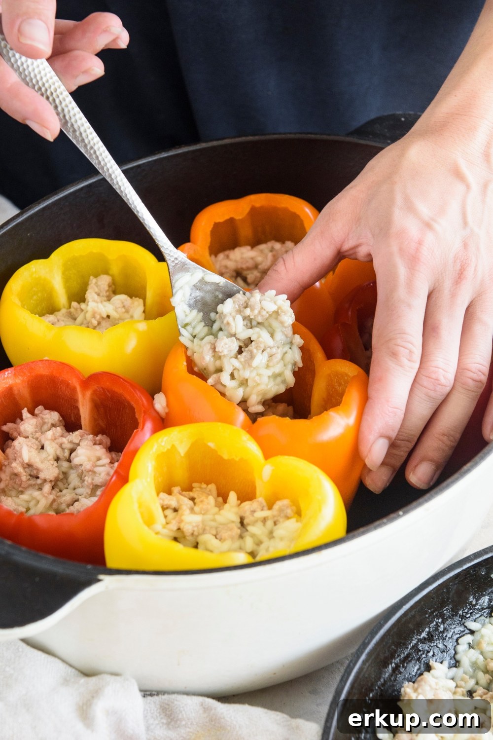 Old-Fashioned Stuffed Bell Peppers Recipe 7 A person using a spoon to stuff bell peppers with a rice and ground meat mixture.