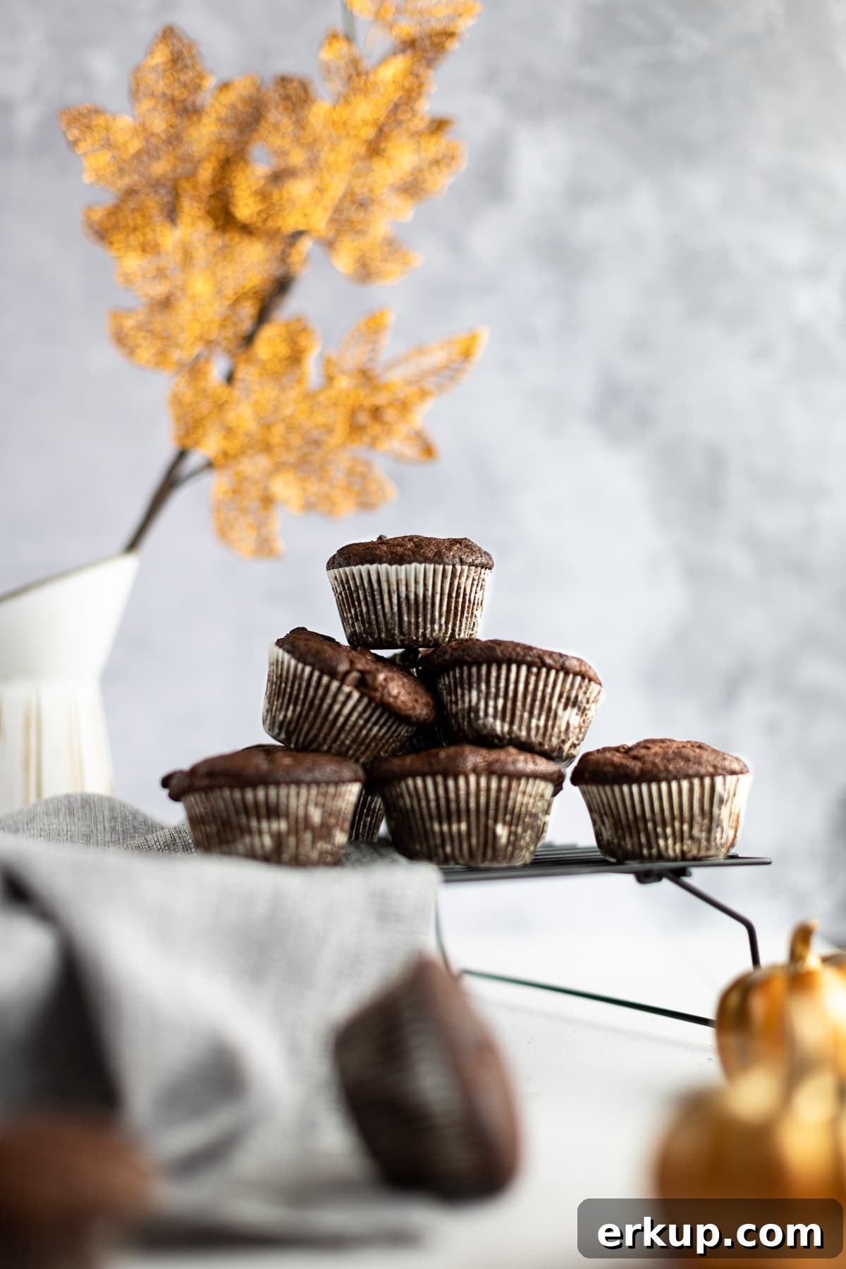 High-Protein Pumpkin Muffins Recipe 2 A pyramid of pumpkin protein muffins sitting on a wire cooling rack, with golden shiny leaves in the background.