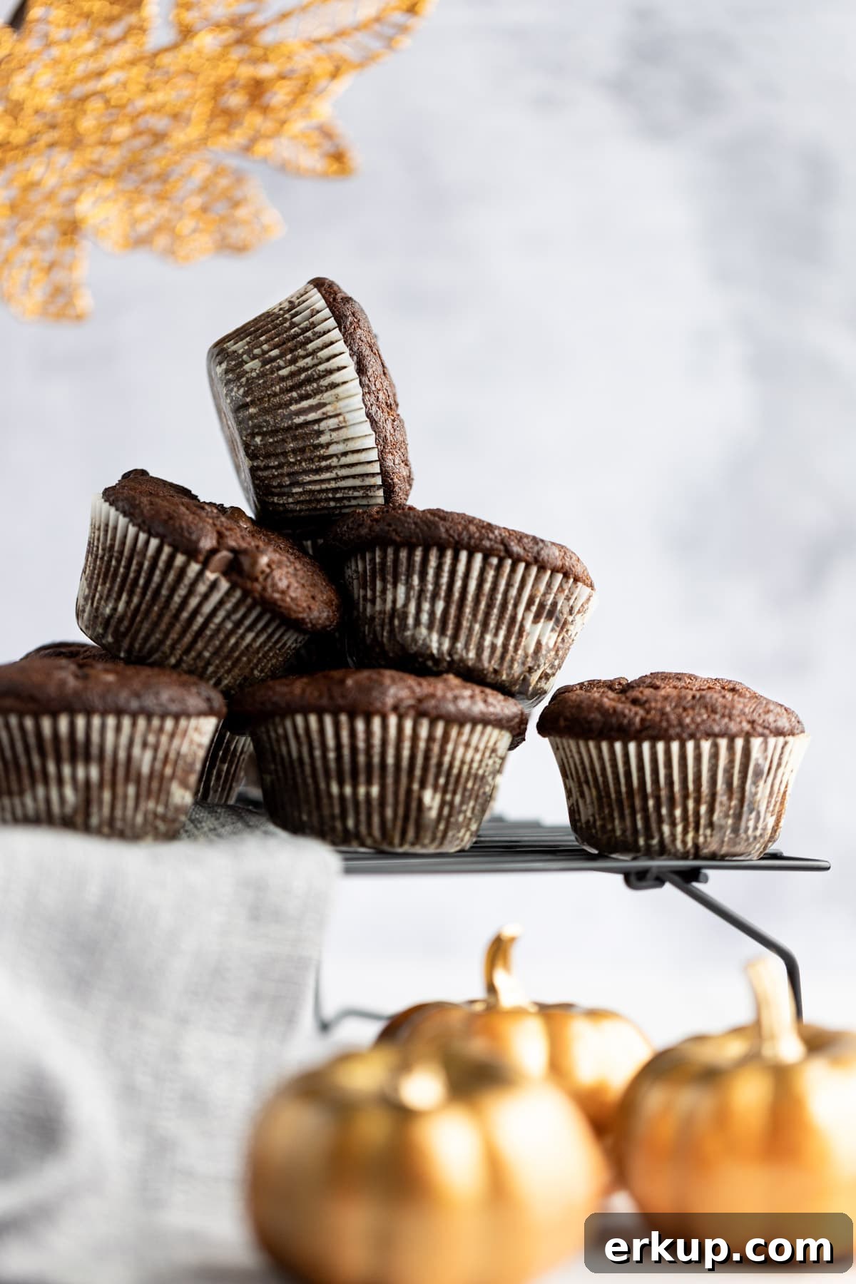 High-Protein Pumpkin Muffins Recipe 4 Up close view of a stack of protein muffins on a black wire rack, with a stack of golden pumpkins in front.