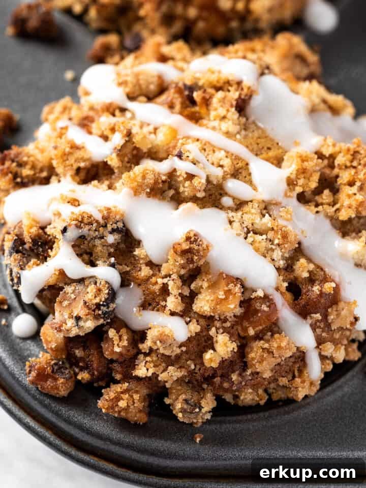 A banana and white chocolate muffin in a muffin tin, with a streusel topping, drizzled with white glaze.