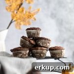 A stack of pumpkin protein muffins on a black wire rack, with a vase of golden leaves in the background.