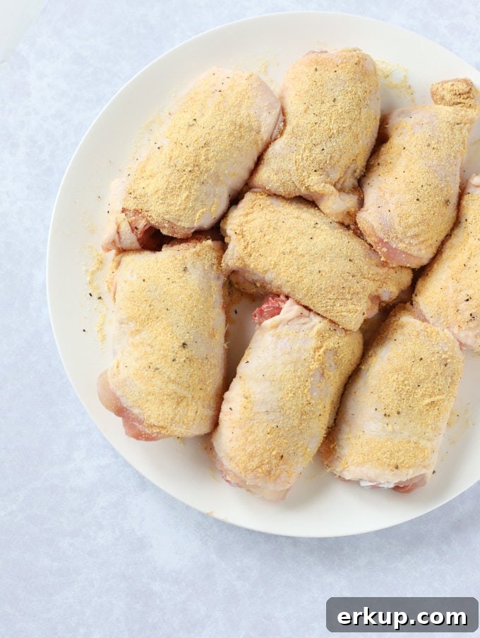 Raw chicken thighs on a plate rubbed with garlic powder.