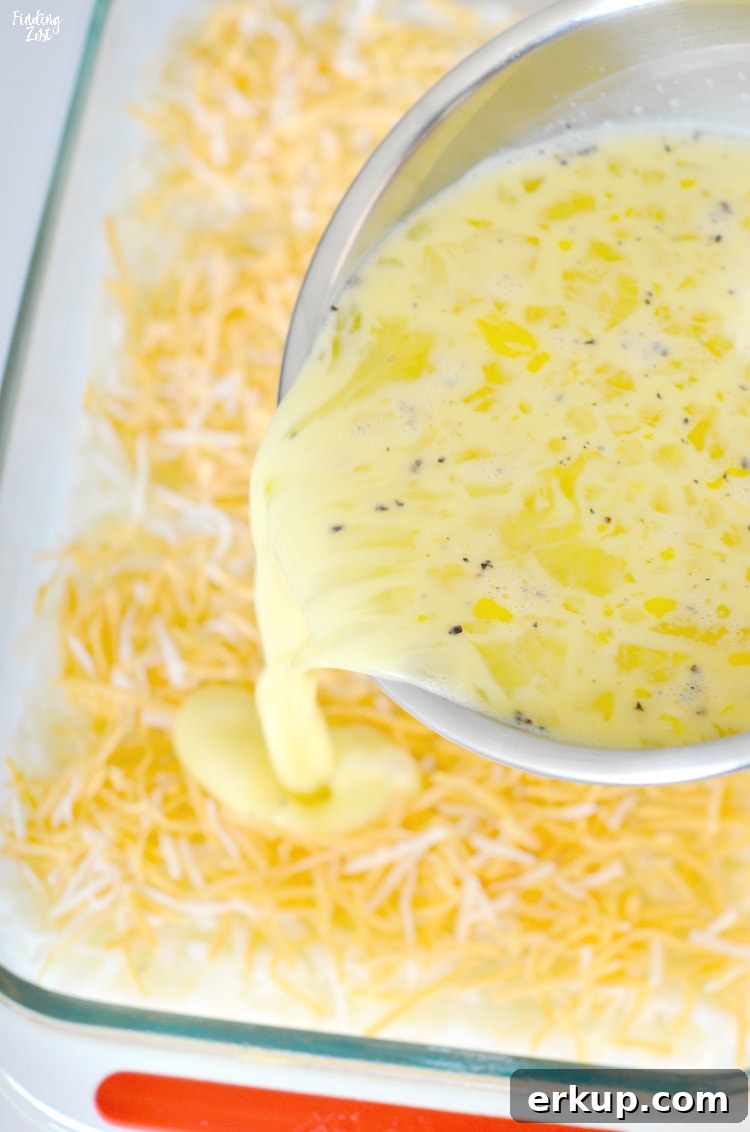 Pouring eggs over hash browns and cheese before baking