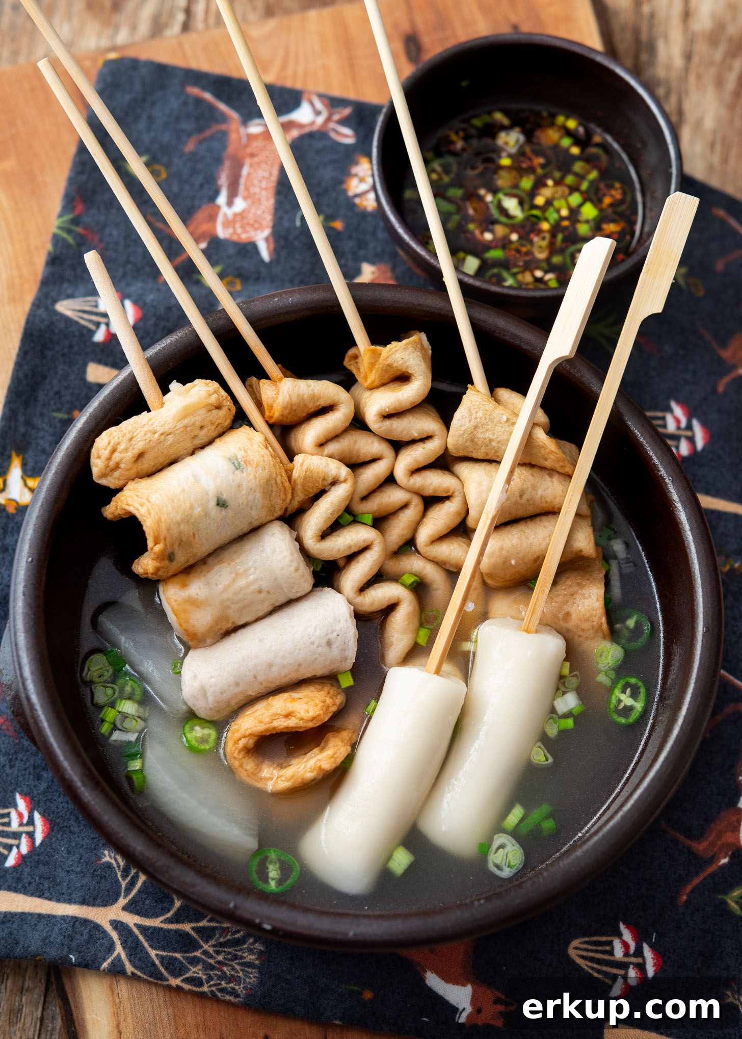 Skewered fish cakes (eomuk) served in a light Korean broth and a small bowl of dipping sauce on the side.