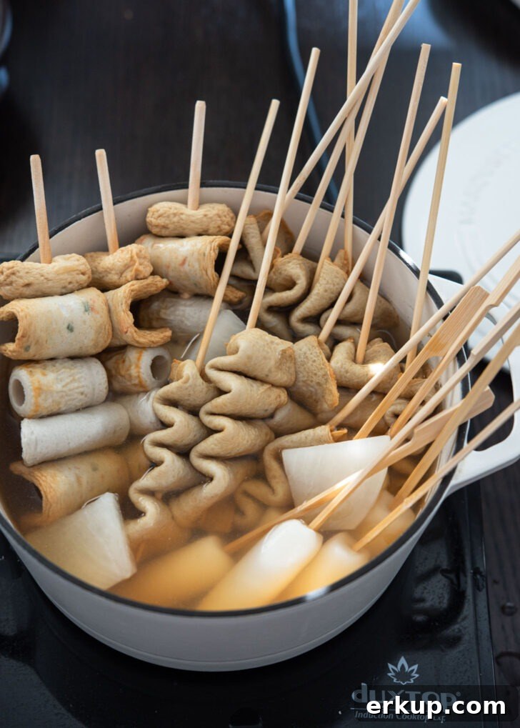 Fish cake and rice cake skewers simmering in Korean soup broth in a pot.
