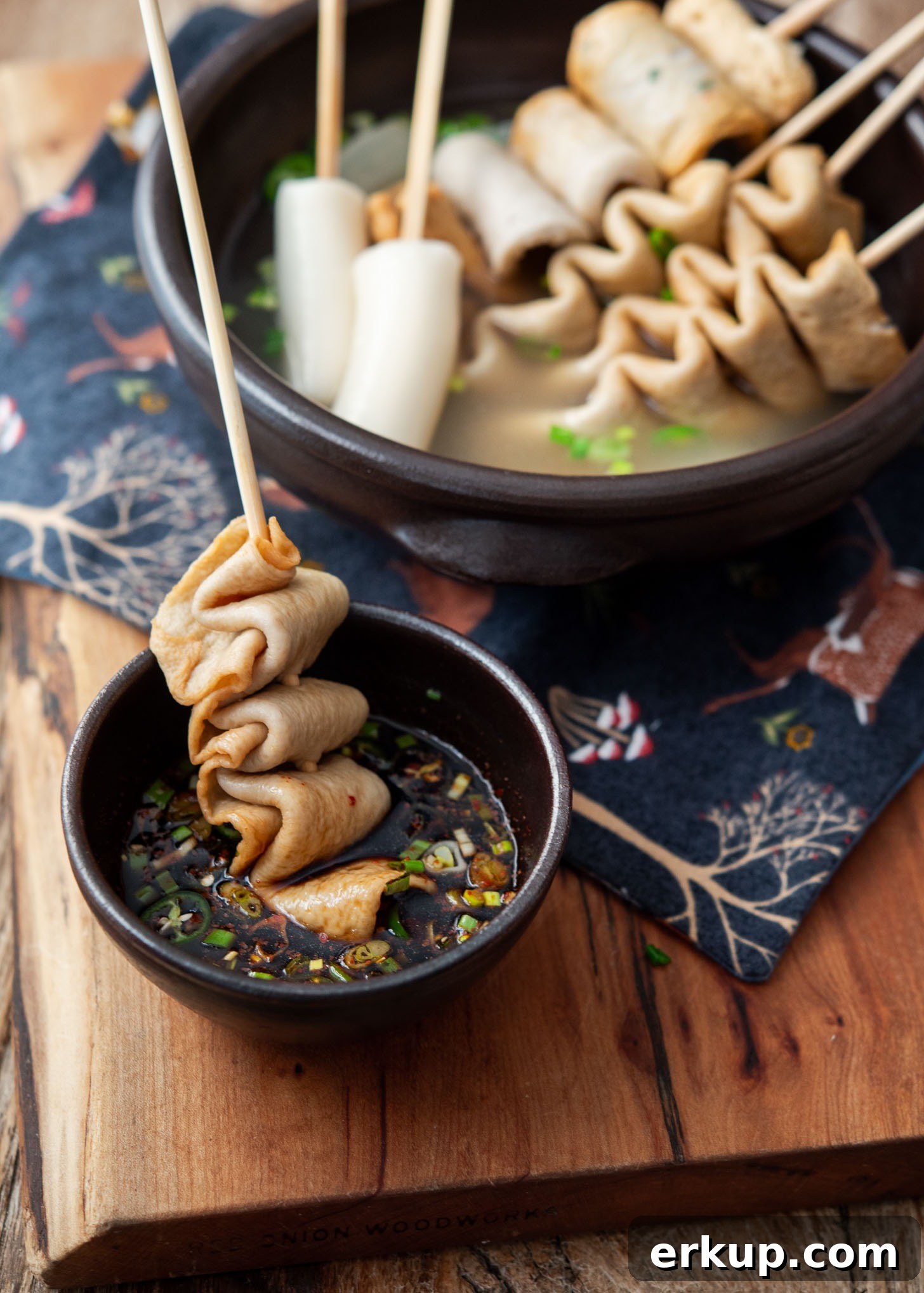 Flat fish cake skewers (eomuk) being dipped into a soy-based Korean chili sauce for serving