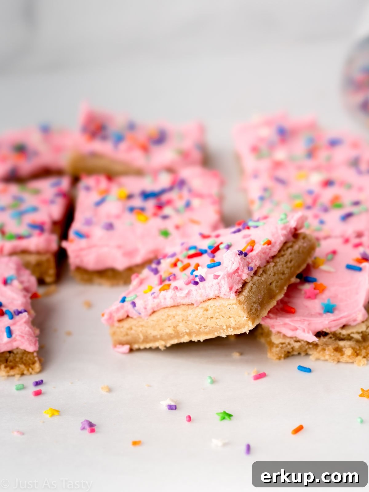 Pink frosted sugar cookie cake bars on parchment paper. 