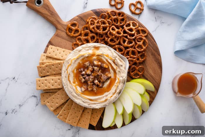 Overhead view of a bowl of snickers dip surrounded by various dippers on a wooden board.