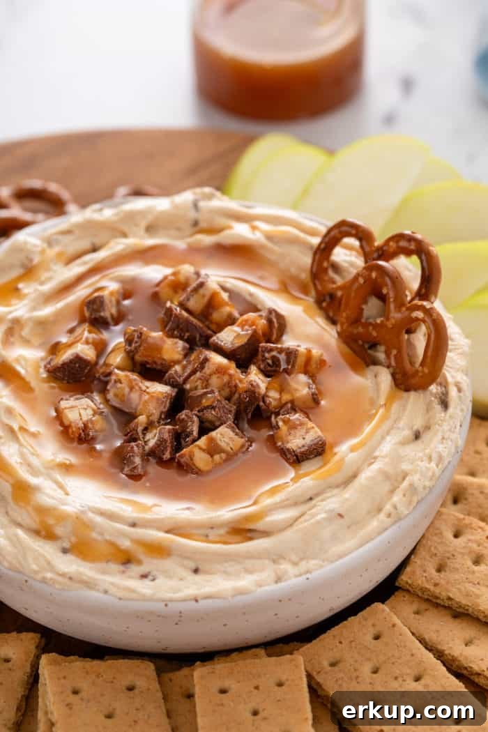 Close up image of a bowl of snickers dip with pretzels stuck in it.