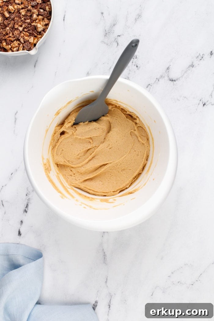 Peanut butter and cream cheese base for snickers dip mixed in a white mixing bowl.