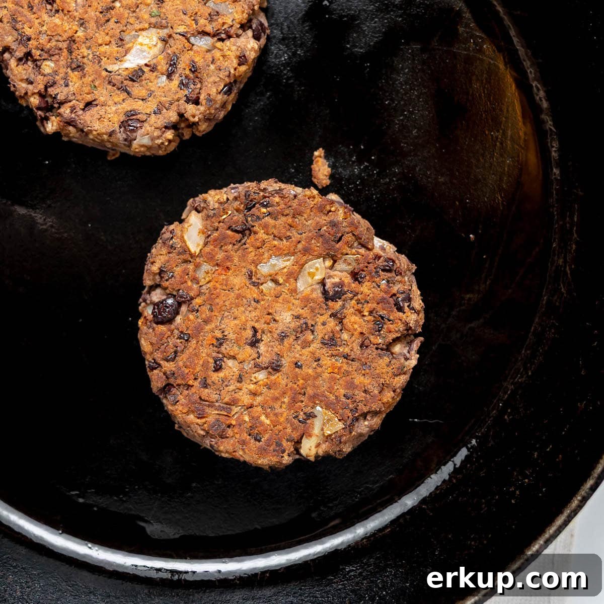 Two cooked black bean patties sit on a black cast iron skillet.