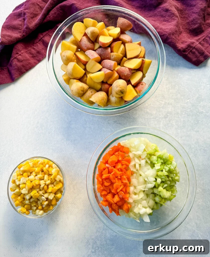 raw potatoes, corn, carrots, celery, and onions in separate glass bowls