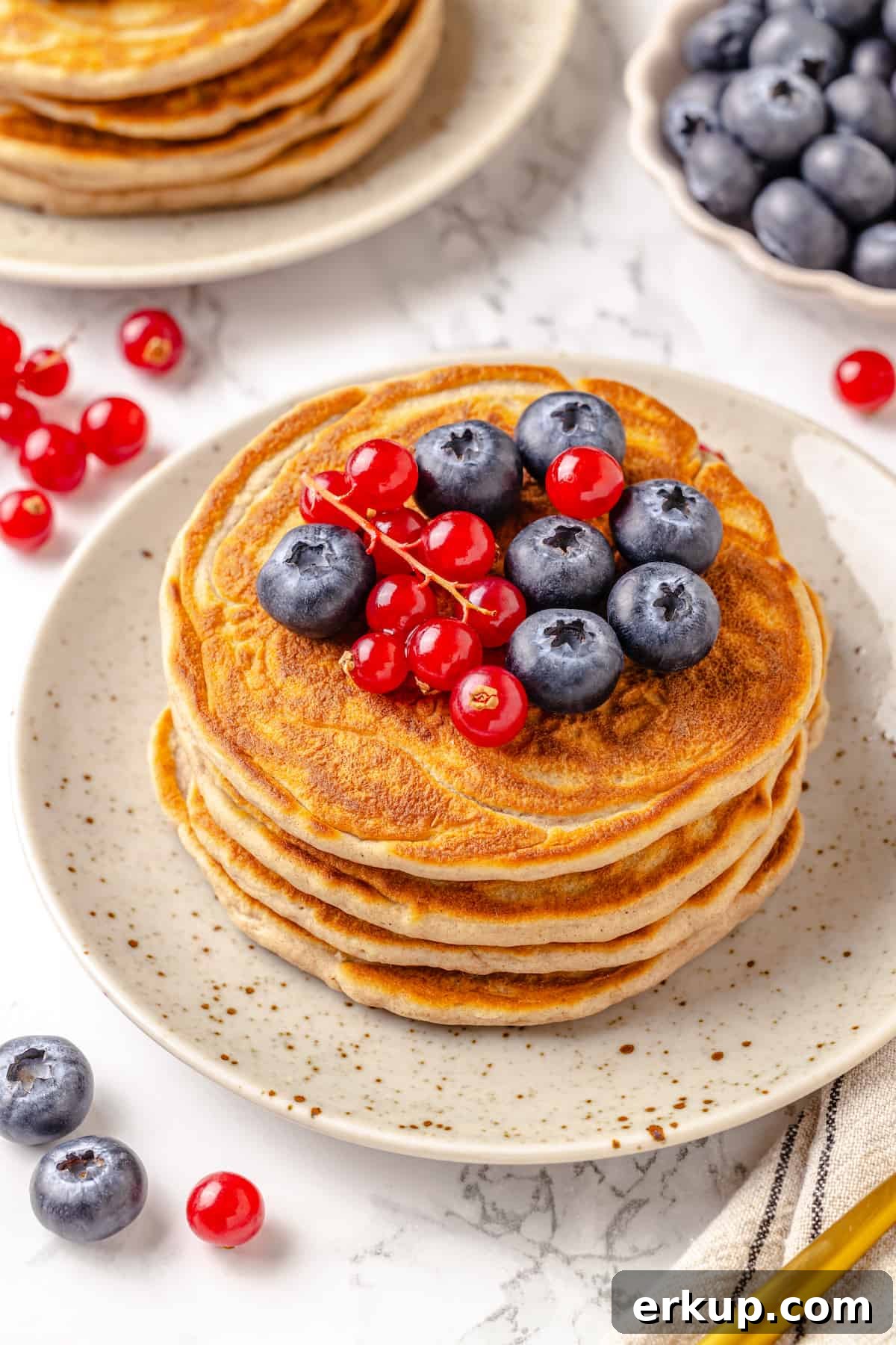 Stack of protein pancakes on plate with fresh berries on top