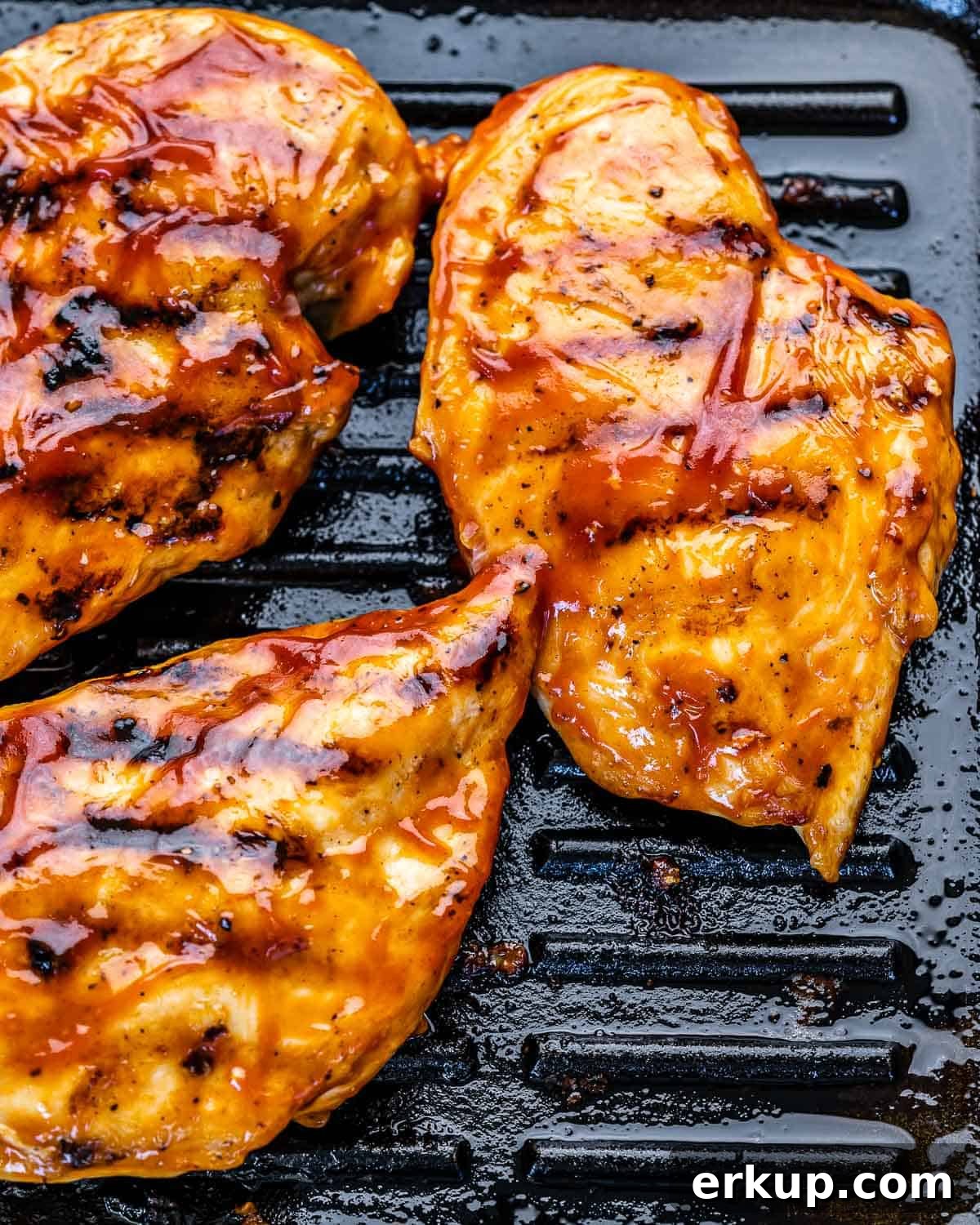 three chicken breasts on grill pan with BBQ sauce