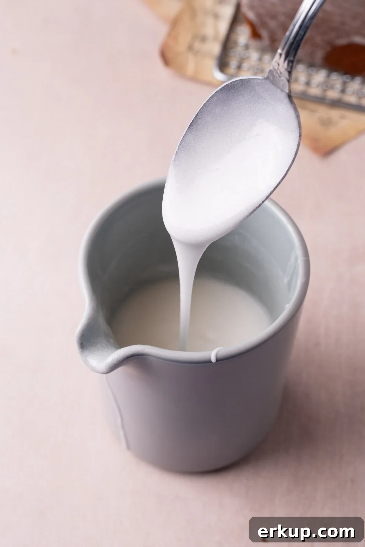 Silky Pourable Coconut Glaze for Cakes and Pastries 2 Coconut glaze running off a spoon into a creamer.